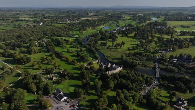 Adare, County Limerick, Ireland, September 2024. Drone orbits counter clockwise showcasing the main street with abbey, friary, and castle ruins as river Maigue winds through the countryside.