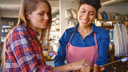 Close Up Of Female Sales Assistant With Digital Tablet Helping Customer In Gift Shop Or Store