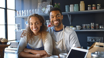 Portrait Of Smiling Young Couple Running Coffee Shop Standing Behind Counter