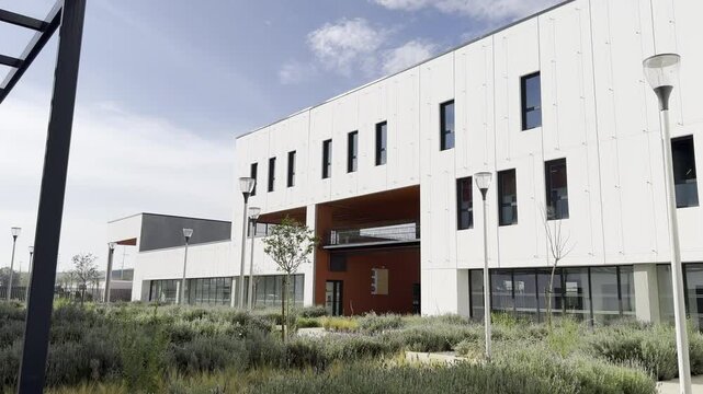 Modern white building with red accents, landscaped greenery, and outdoor pathways under clear skies