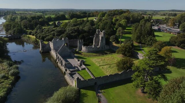 Desmond Castle, Adare, County Limerick, Ireland, September 2024. Drone orbits clockwise and descends towards the River Maigue with the 13th century Norman ruin by the water with shimmering reflections