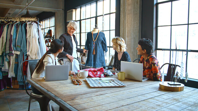 Four Female Fashion Designers In Studio Meeting Discussing Garment On Dummy