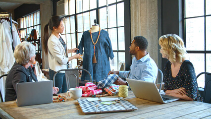 Male And Female Fashion Designers In Studio Meeting Discussing Garment On Dummy
