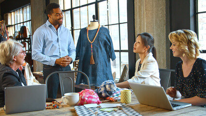 Male And Female Fashion Designers In Studio Meeting Discussing Garment On Dummy