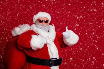 Photo of body positive santa show thumb up carry big bag with presents wear hat eyewear coat isolated on red background