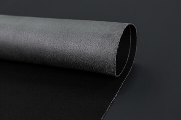 A close-up of a rolled-up piece of gray automotive fabric, showcasing its smooth texture and durability. This high-quality material is commonly used for car interiors.