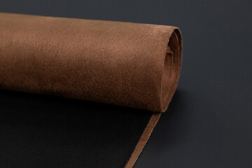 A close-up of a rolled-up piece of brown automotive suede fabric, showcasing its soft texture and luxurious appearance. This premium material is often used for high-end car interiors.