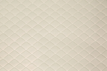 Fototapeta premium A close-up of a cream-colored automotive fabric with a diamond-shaped pattern. The fabric has a soft, luxurious, and vintage-inspired appearance.