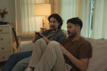 Two Men Playing Video Games Together on Couch in Cozy, Dimly Lit Room