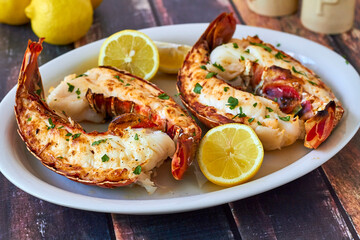 broiled rock lobster tails served with butter and fresh lemon on a white plate