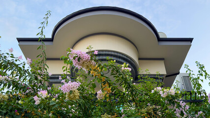 Photo of Modern Architectural Facade and roof with Floral Greenery and Curved Design. A contemporary building surrounded by vibrant bougainvillea flowers under a serene sky.