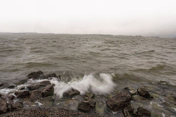 Waves crash against rocky shore under overcast sky in coastal landscape during early morning hours
