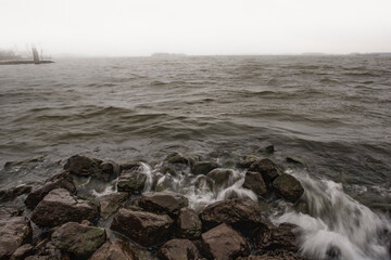 Waves crash against rocky shore under overcast sky at coastal location during early morning hours