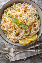 Creamy spaghetti with ricotta cheese, lemon zest and juice, parmesan, pepper and basil close-up in a bowl on the table. Vertical top view from above