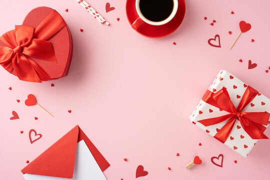 Top view of valentines day gifts wrapped with red ribbons and hearts, accompanied by a coffee cup on a pink background