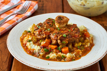 osso bucco served over mashed potatoes topped with a mixed vegetable gravy