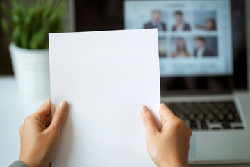 Obraz premium Hands holding blank resume sheet in front of laptop with plant. This conveys sense of preparation and professionalism in job application context