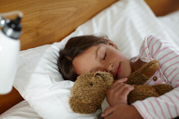 Girl, child and sleeping in bed with bear, toys and tired with rest, dream and wellness in family...