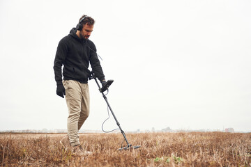 Cloudy white background. Man is with metal detector in the field