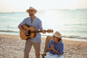 retired, retirement, couple, senior, elderly, beach, recreation, insurance, planning, vacation. A man and woman are playing guitar on a beach. The man is smiling and the woman is laughing.