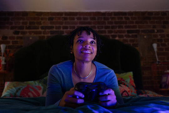 Young adult female playing a video game at home in her bedroom at night