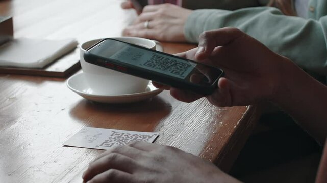 Close-up shot of unrecognizable man using camera on his smartphone, scanning QR-code, accessing menu, while sitting in cafe during coffee break
