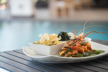 Plate of grilled prawns served with Sri Lankan yellow rice and kangkung by the poolside
