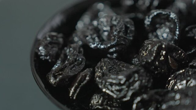 A black prune rotates on its axis in a black cup. The shot is close-up with a shallow depth of field.