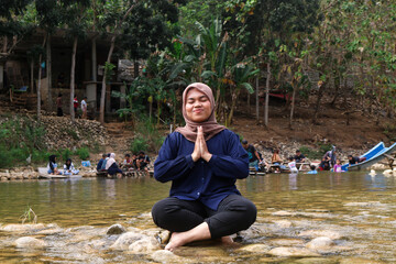 Young woman practicing morning meditation and yoga while sitting in lotus position, meditating on river rocks in nature. meditation or woman with prayer hands in nature