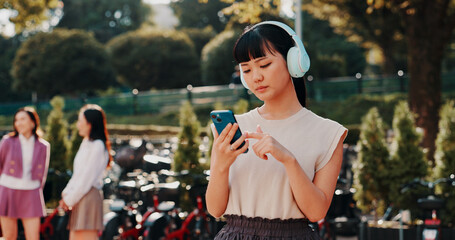 Fototapeta premium Headphones, phone and college with Japanese woman in park for streaming, University campus and online playlist. Music, radio and education podcast with person and mobile in Japan outdoor for student