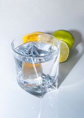 A transparent glass glass with water stands on a white table, next to it there is a lemon and a lime.
