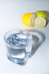 glass transparent glass with water stands on a white background next to lemon and lime