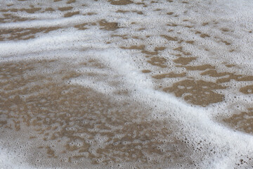 Detailed view of foamy sea water gently covering the sandy beach, highlighting natural textures and...