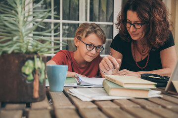 Astonished student doing homework at home with school books newspaper, digital pad helped by his...