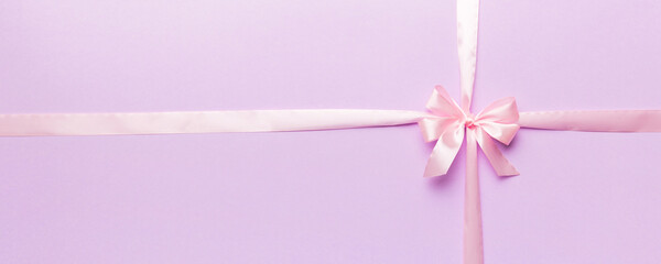 Top view of purple ribbon rolled and pink bow isolated on colored background. Flat lay with copy space