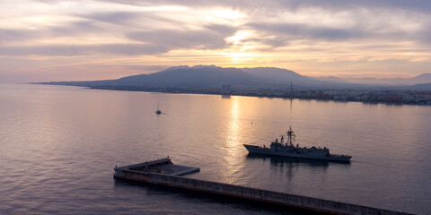 Serene maritime scene: Ship near pier at sunset with mountain reflections, calm waters, and a picturesque sky.  travel, nature, or tranquility concepts in stock photography.