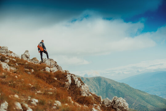 A male climber standing on the top of rocky mountain peak cliff, adventure travel, extreme sport outdoor.