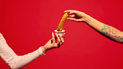Human hand holding sweet delicious churros and dipping into berry jam against red background....