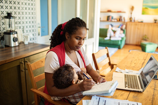 Multitasking mom breastfeeding while working on laptop at home