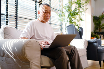 Old man using laptop sitting and working on the sofa.