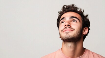 Fototapeta premium Young Man Looking Up with Hopeful Expression Against Plain Background