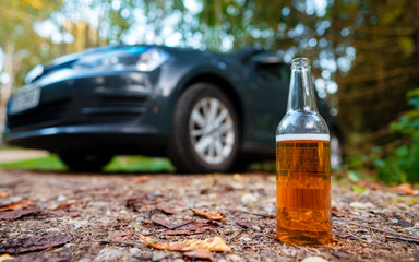 Open bottle of beer in front of a car. Drunk driving concept.