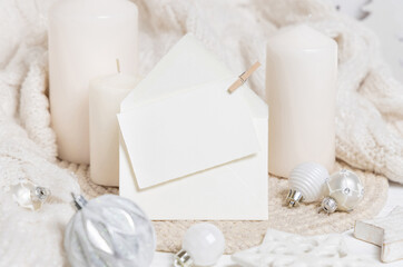 Paper card and envelope near candles, white sweater and Christmas decor, holiday mockup