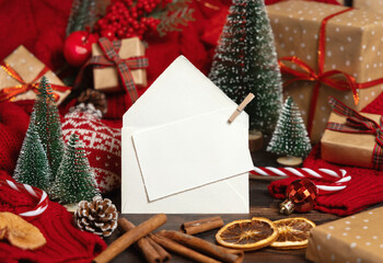 White postcard and envelope near Christmas decor, trees, spices and red sweater, mockup