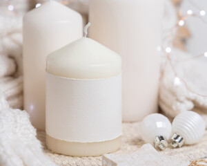 Pillar candle with label near white sweater and wooden Christmas decor, mockup
