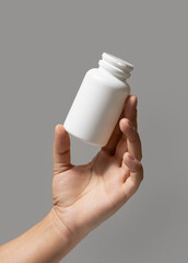 Female hand holding a white plastic pill bottle closeup against grey, Healthcare concept