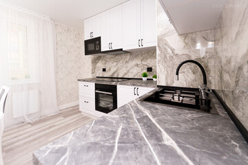 modern kitchen apartment interior design. white kitchen with marble countertop and black sink, stove and hood