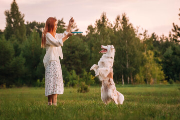 a beautiful red-haired girl in light clothes and sneakers plays a Frisbee disc with her Australian...