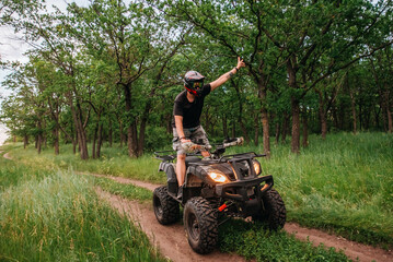a girl and a guy bikers ride quad bikes in a beautiful green forest on a river cliff, their dogs are running nearby © Julia Suhareva