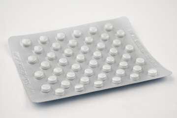 Close up photograph of a pile of white round shaped vitamin, tablets or pills in package. isolated on white background. 